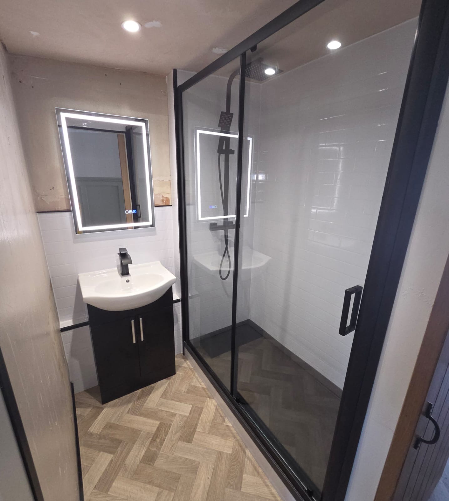 Compact shower room with black framed enclosure, LED mirror and herringbone flooring